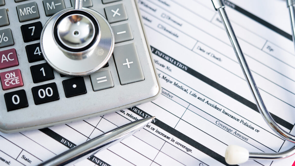 A photo of health insurance paperwork with a stethoscope and calculator resting on top.