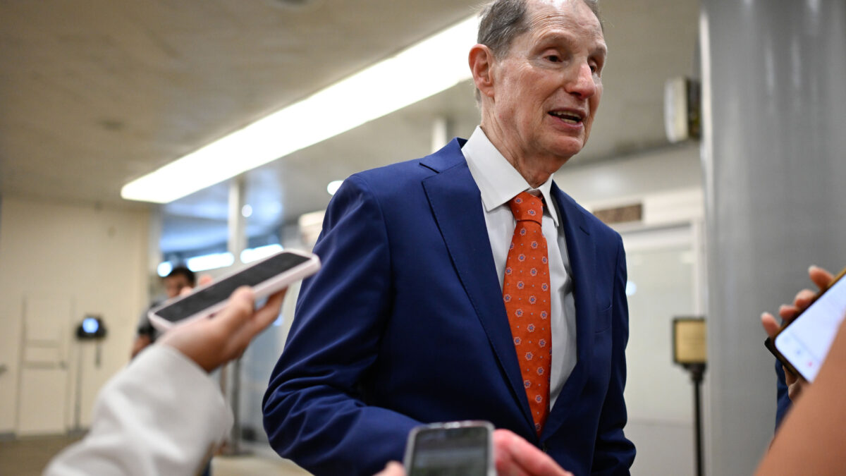 Senator Ron Wyden walks past a few reporters, who hold up their cell phones as recording devices as he speaks in passing.