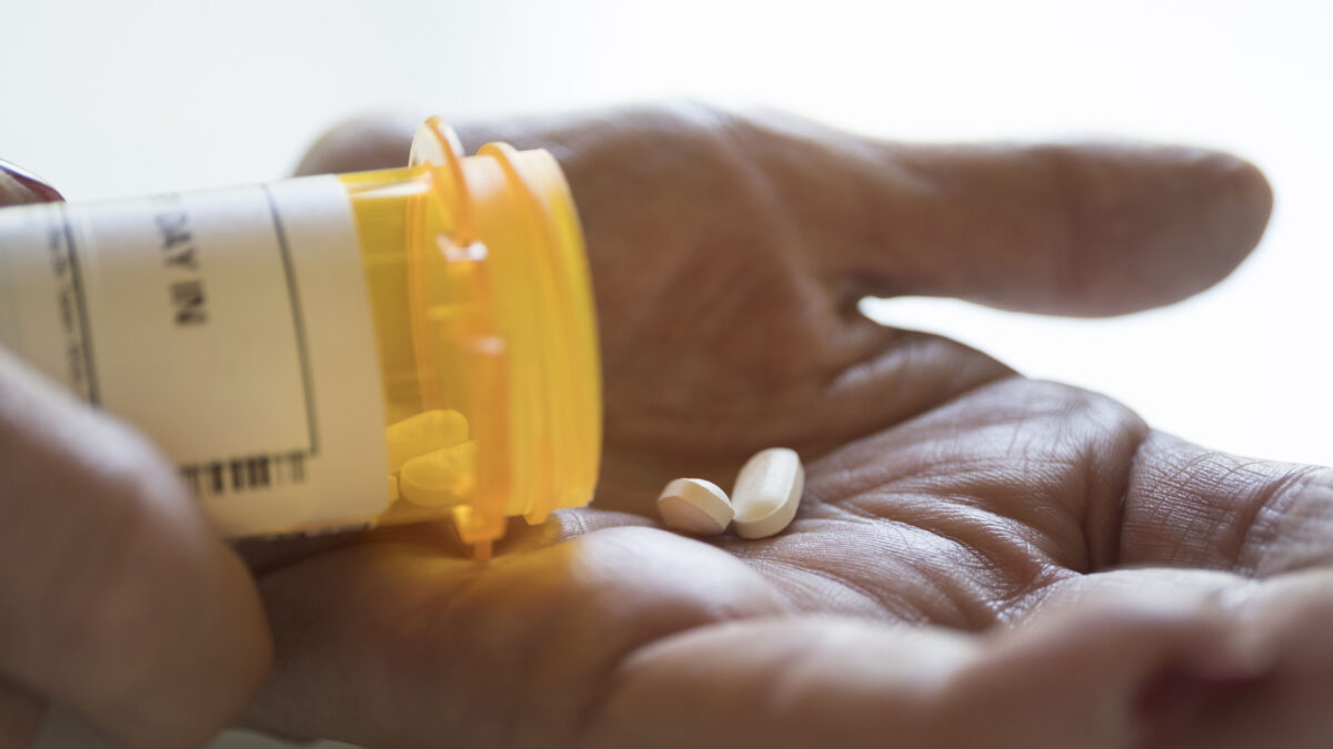 A close-up shot of a hand holding two pills that have been dropped out of an orange pill bottle.