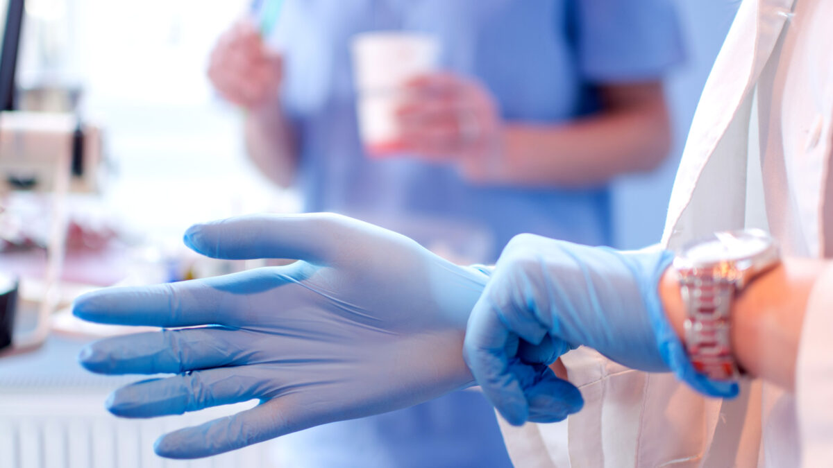 A close up photo of a doctor's hands putting on blue sterilized surgical gloves in a medical setting.