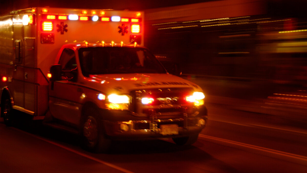 A photo of an ambulance with lights on speeding along the road at night.