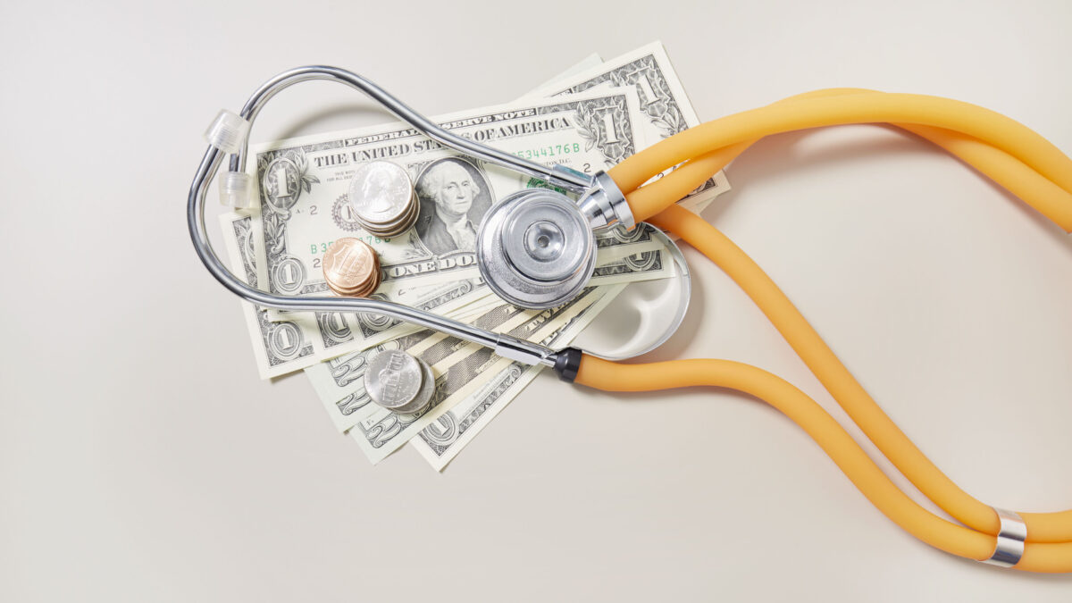 A high angle view of American dollar bills and coins with a stethoscope resting on top of them.