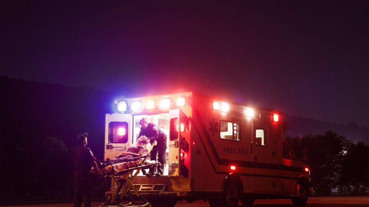 A photo of an ambulance. Paramedics load a patient on a gurney into the ambulance.