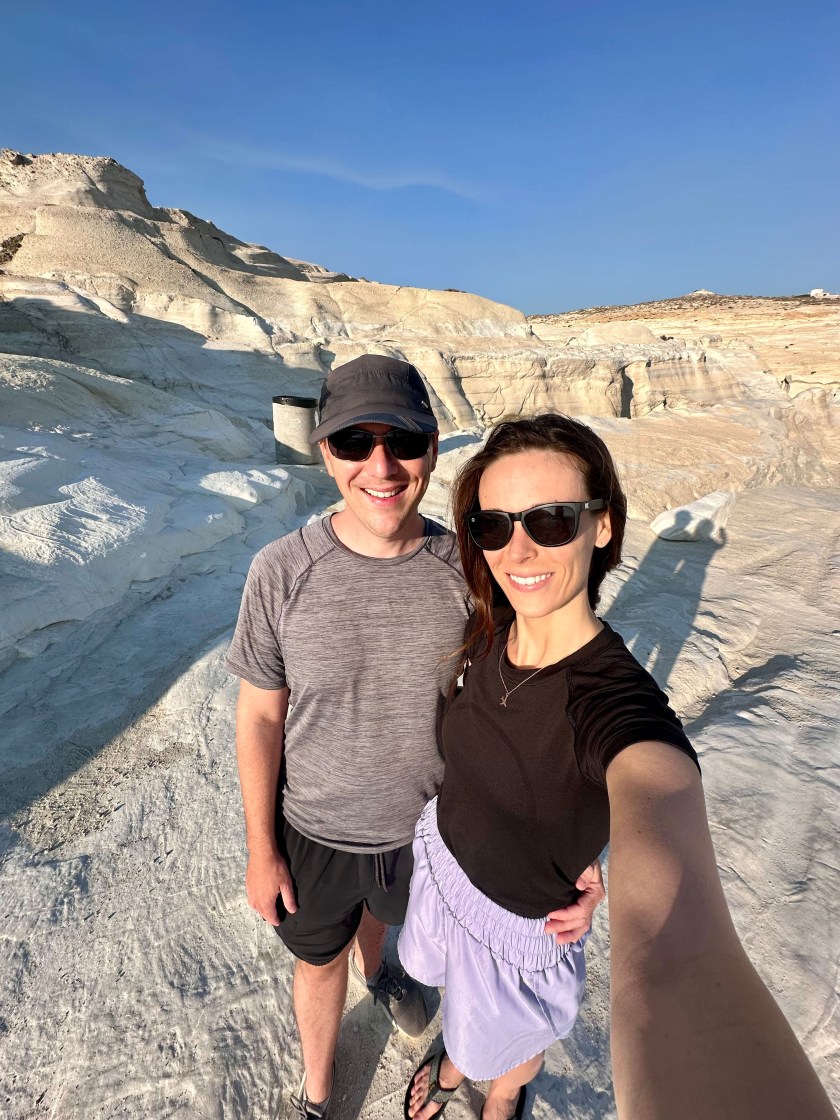 ivf-tourism-solomon-01 A man and woman pose for a selfie on sunny day in a rocky landscape in Greece.