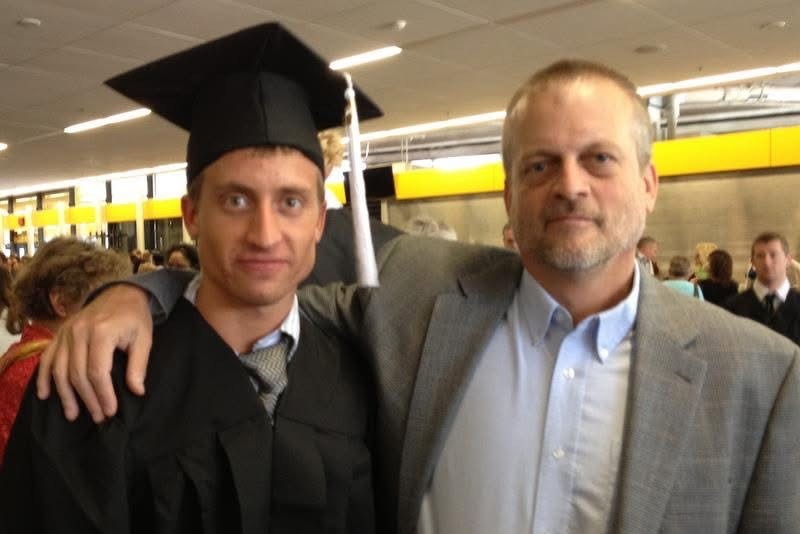 jacobsen A photo of a man in a graduation cap and gown posing for a photo with his father, who has his arm wrapped around his son.