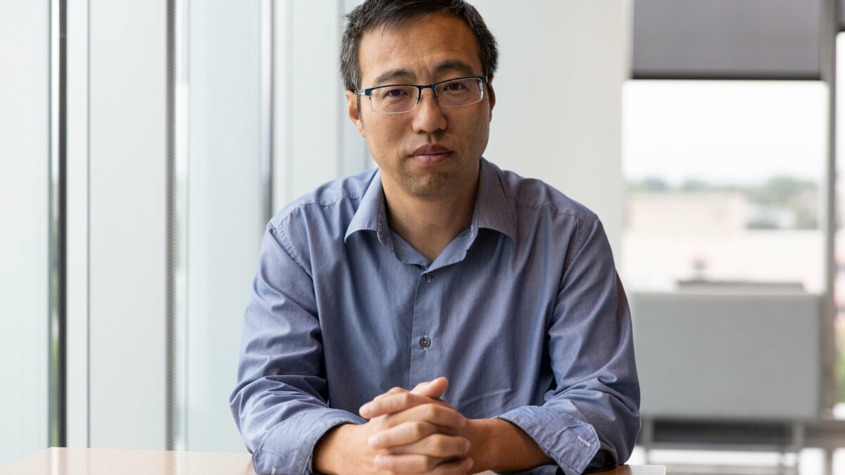 A photo of a man sitting at a desk indoors.