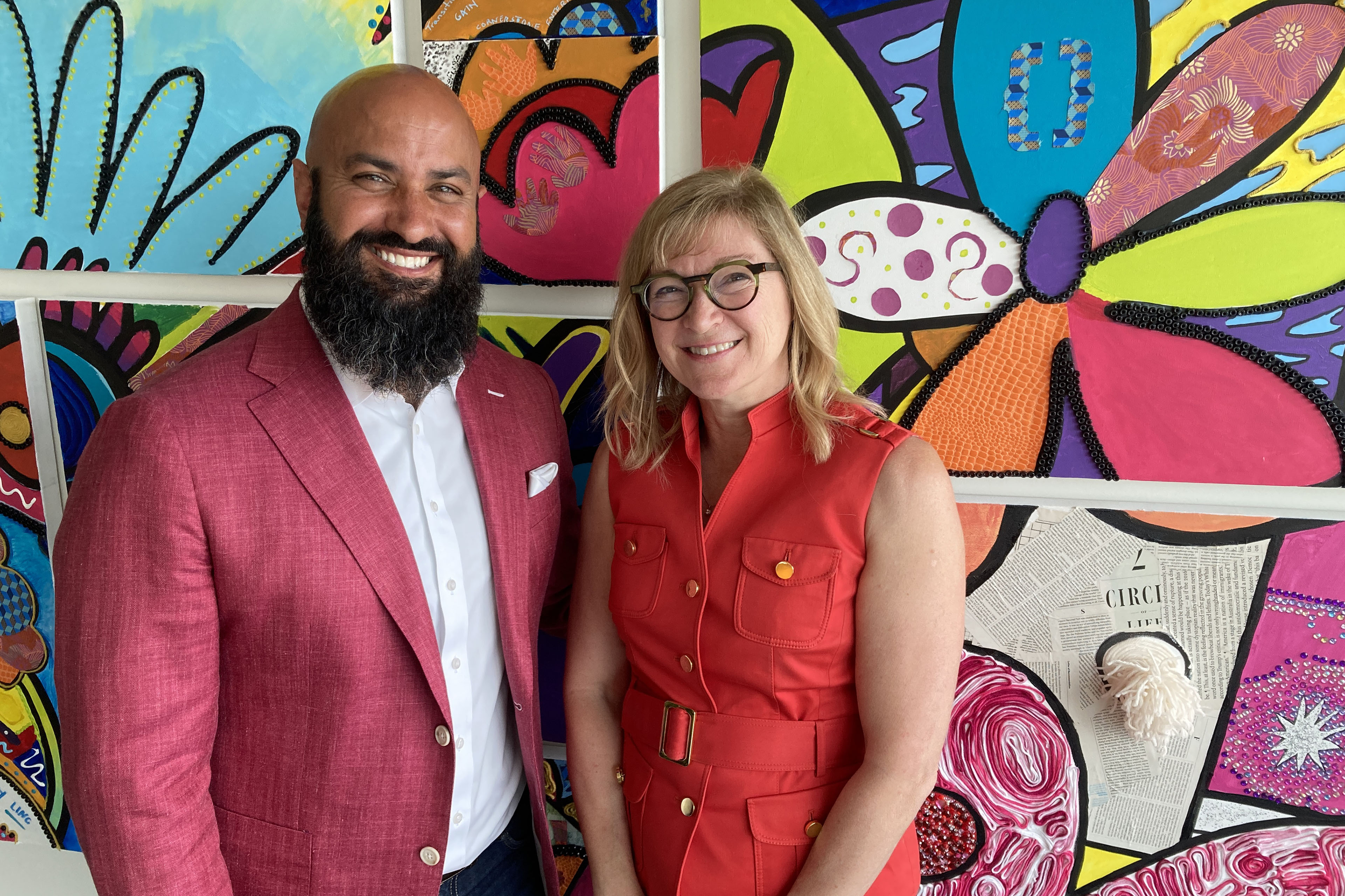 kansas-city-charity-money-07-3840 A man with a beard wearing a red blazer and white shirt stands next to a woman with glasses wearing a red dress. They stand in front of a brightly colored wall