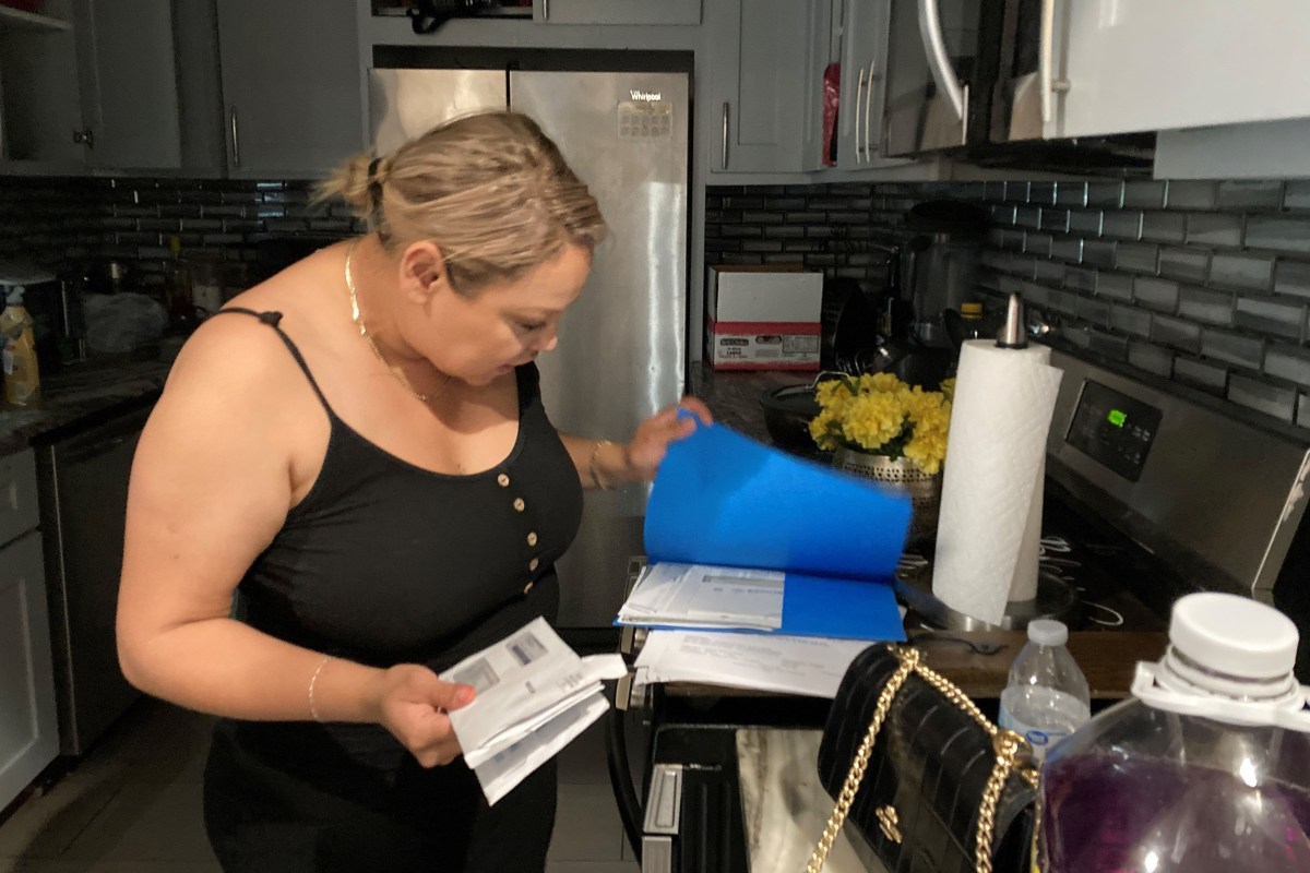 kansas-city-victims-money-arellano-04 Abigail Arellano, standing in her kitchen, looks over a stack of bills in a blue folder.