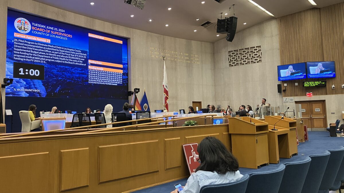 A court room with a large projector screen at the front. There are rows of blue chairs facing the screen.