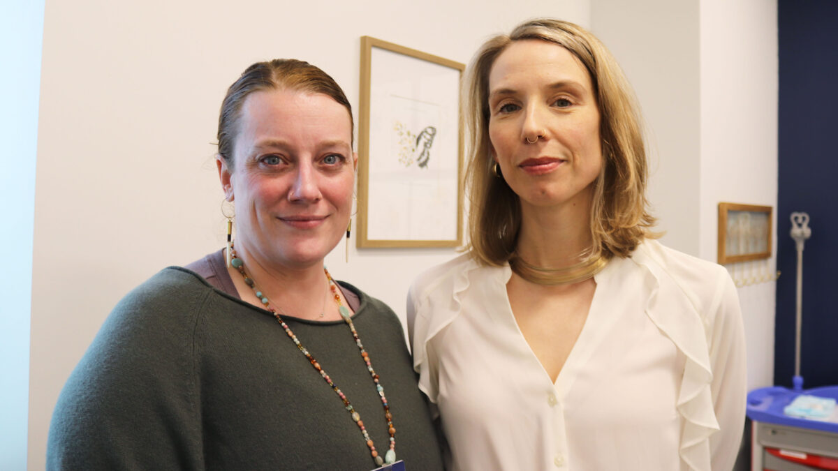 Two women with blonde-ish hair stand side-by-side in a doctor's office.