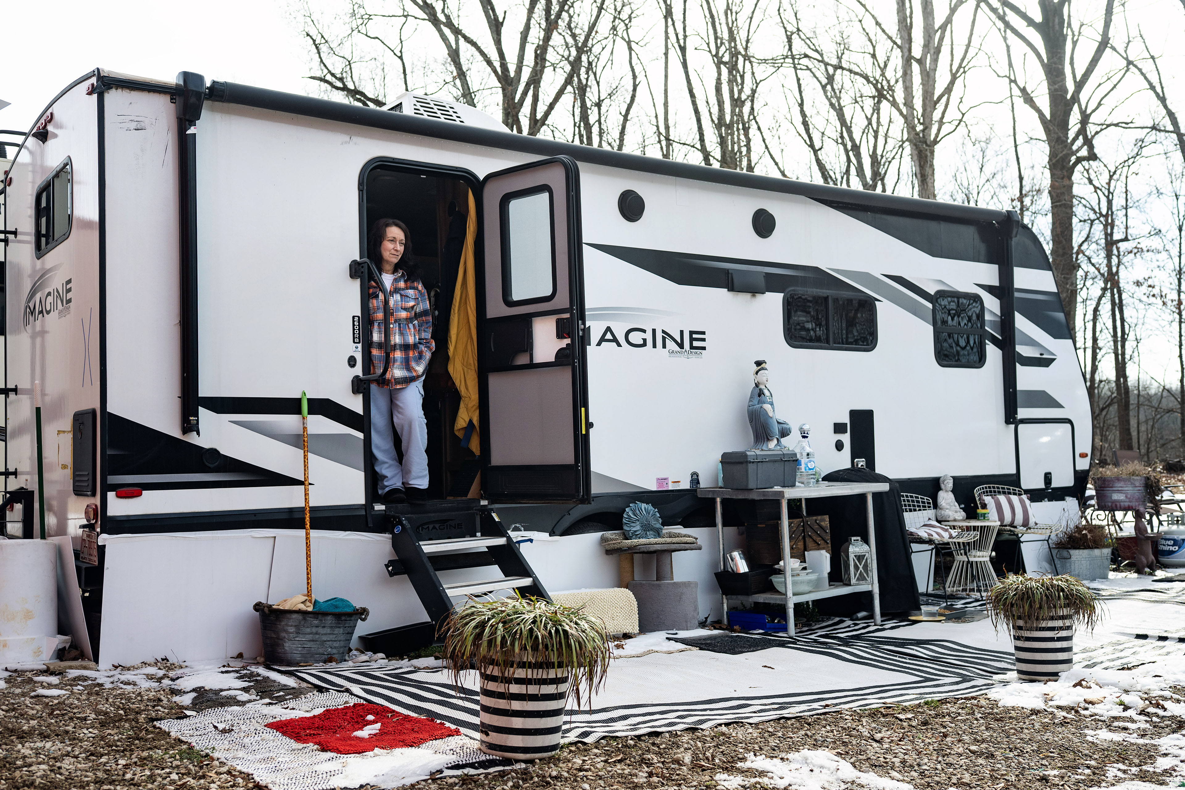 A woman stands in the doorway of her trailer home, facing the outdoors.