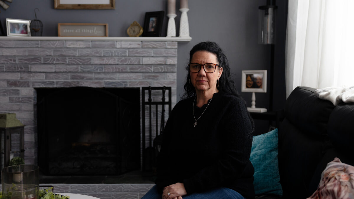 A woman sits on a couch in a living room and looks at the camera.