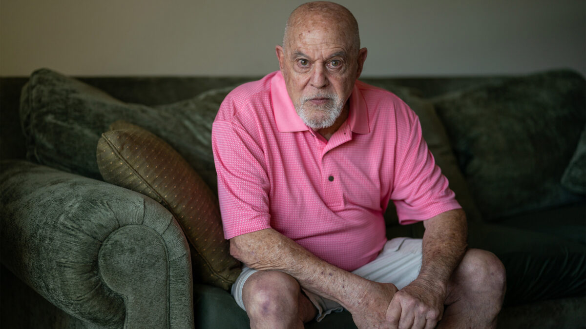 A photo of a man seated on his couch, looking at the camera.