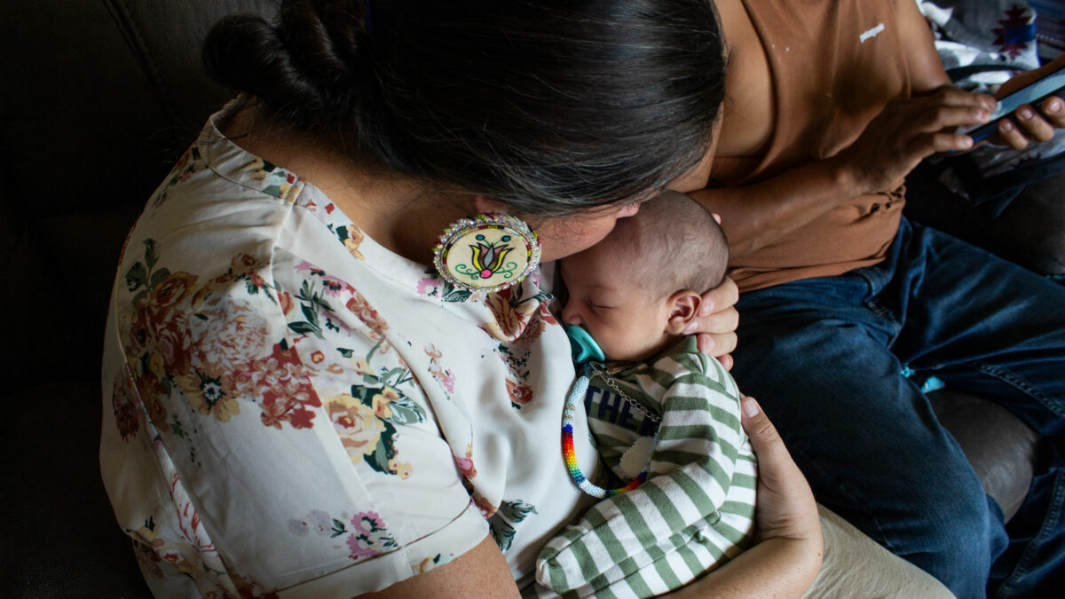 A doula holds a baby while sitting on a couch.