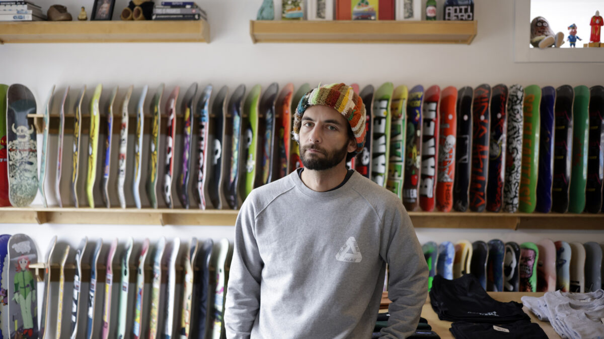 A man wearing a multicolor hat stands in front of two shelves of skateboards