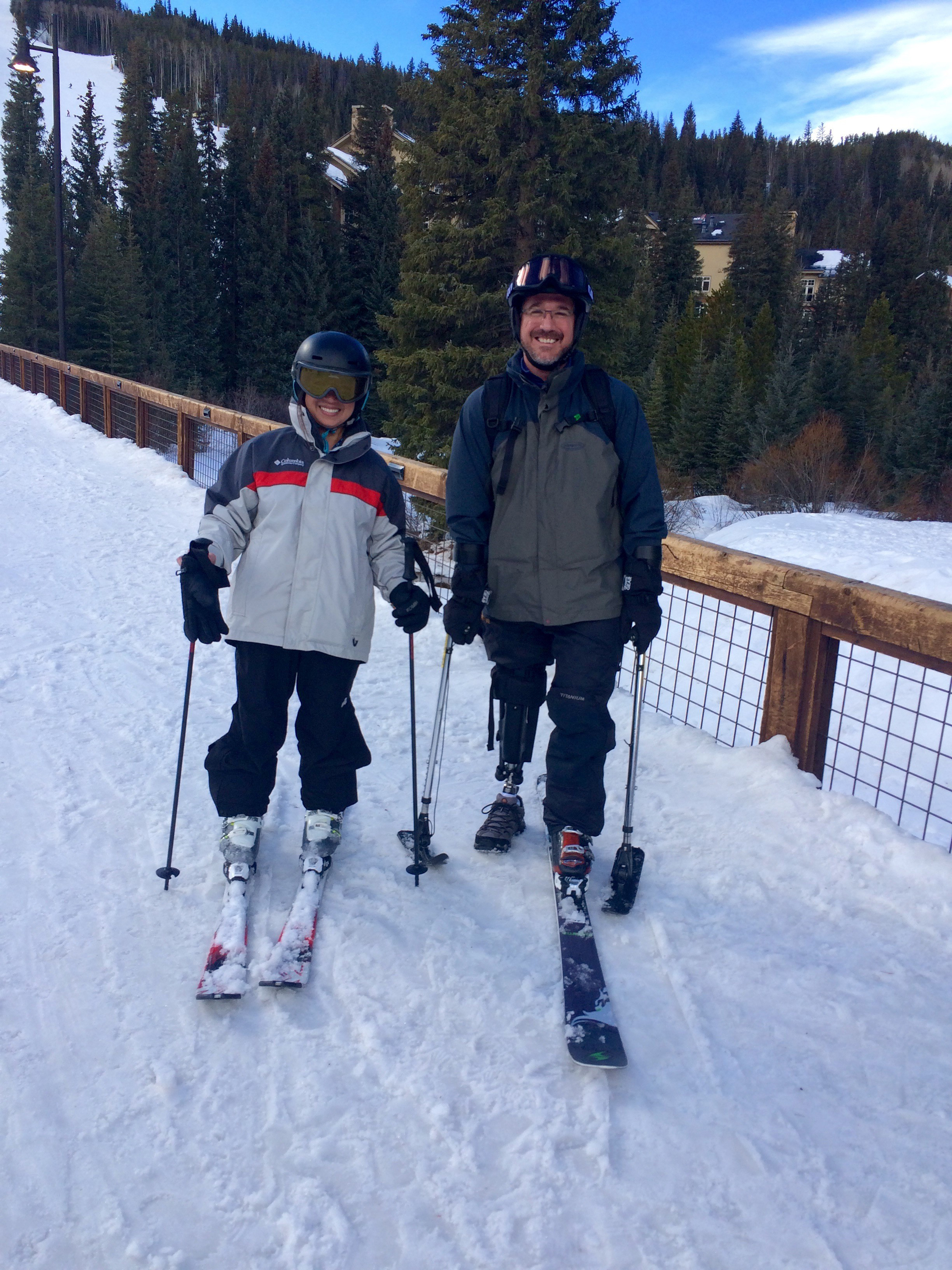 prosthetic-fairness-adams A man with a prosthetic leg stands beside a woman. They are on a snowy ski slope and dressed in snow gear.
