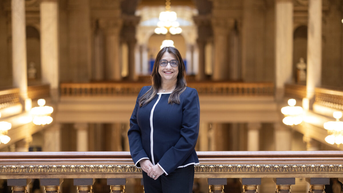 A woman wearing a blue pant suit stands by a balcony in the Indiana state house.