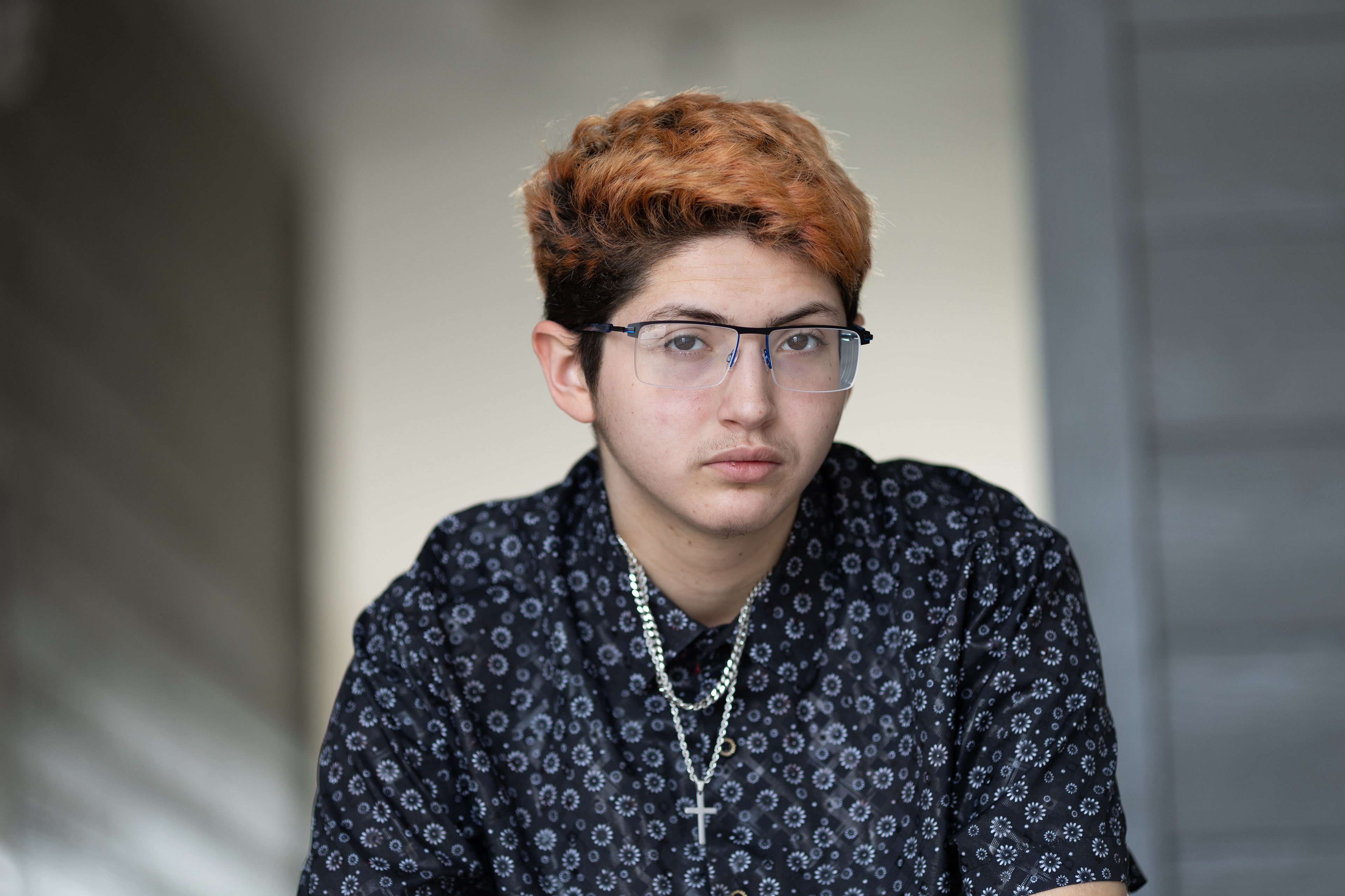 santillan_garciasnap_15 A portrait of a 20-year-old man. He wears glasses and a button-down short sleeve shirt. A silver cross necklace hangs from his neck.