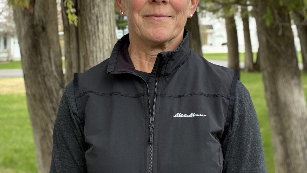 A woman with very short gray hair wearing a black fleece jacket smiles in the direction of the camera.