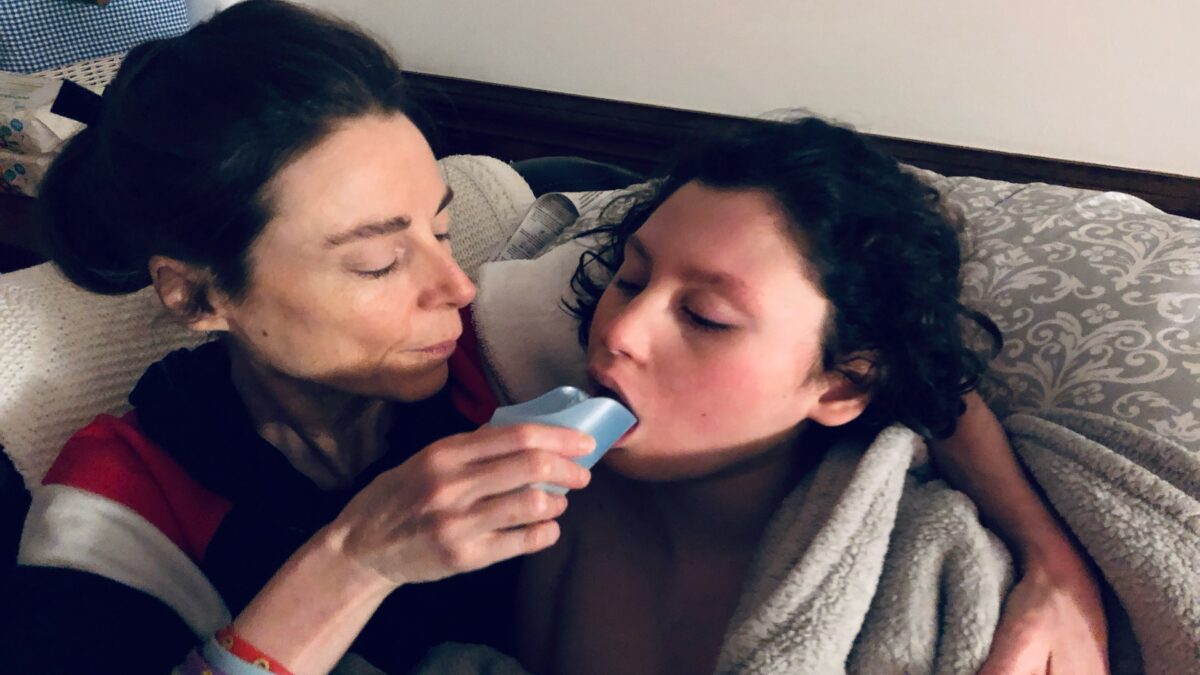 A woman embraces a young boy, feeding him a liquid from a small cup