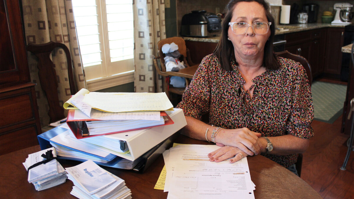 A photo of a woman sitting at a table with a pile of medical records and billing documents.