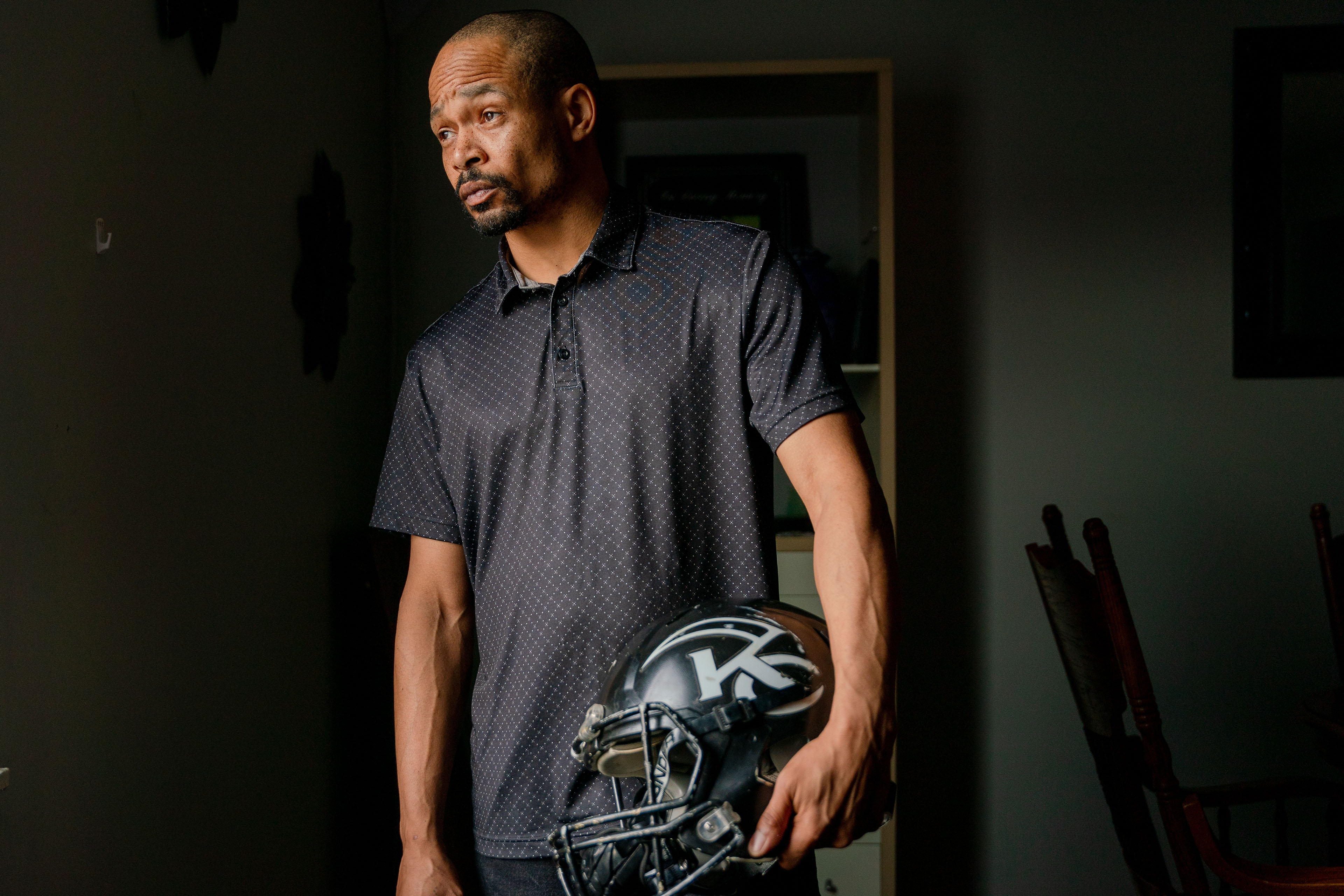 A man in a navy collared shirt poses for a portrait holding a football helmet