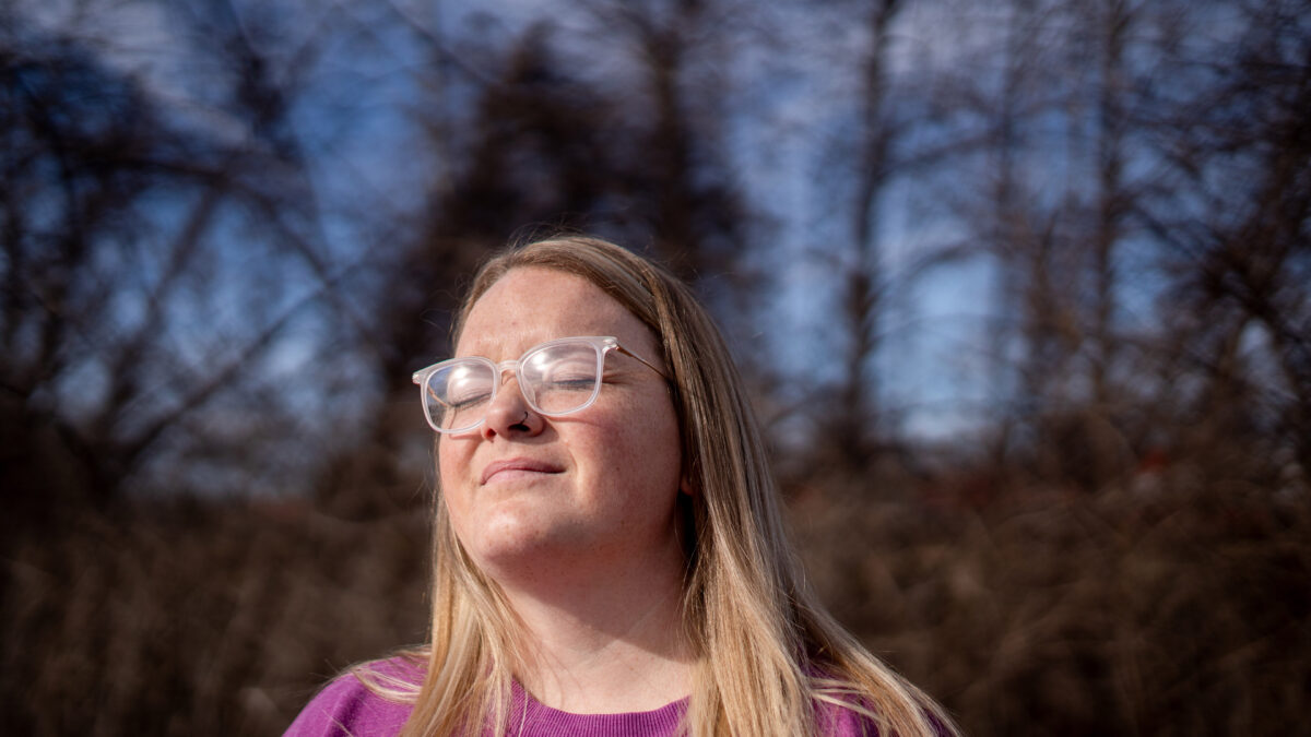 A woman with blonde hair and glasses closes her eyes as she faces the sun