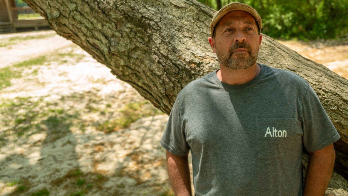 A portrait of a man outdoors, leaning his back against a tree trunk.