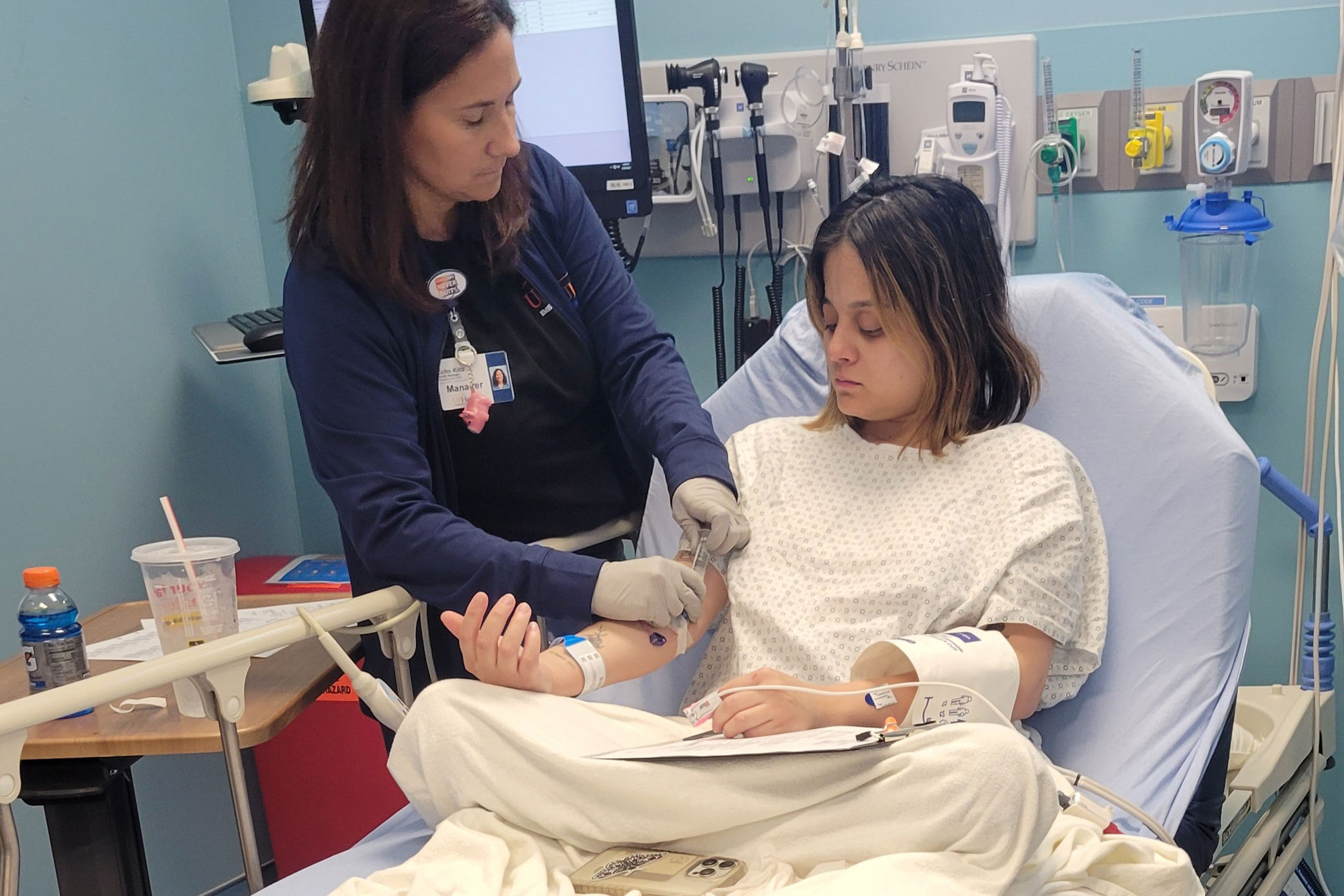 urgenters_05 A female nurse treats a female patient who is sitting in a hospital bed.