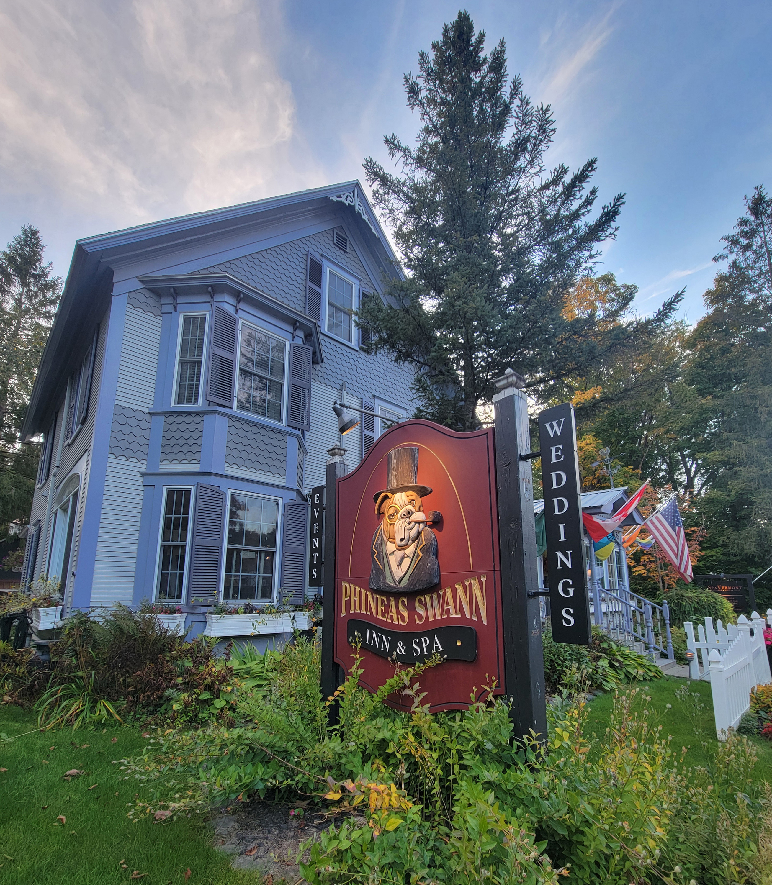 vermont_02-resized A photo of the outside of an inn. A sign outside it has its name above an image of a dog wearing a top hat and monocle, smoking from a pipe.