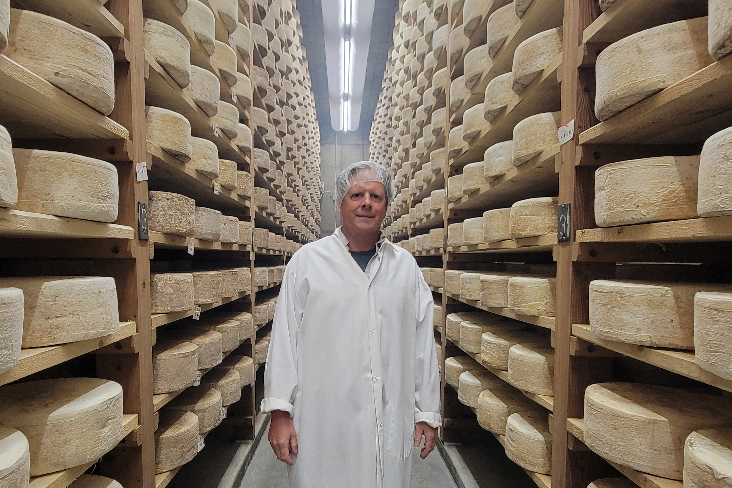 vermont_05-resize A photo of a man standing in a room surrounded by shelves of ripening cheese wheels.
