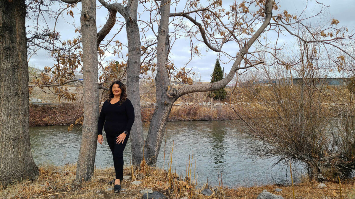 A woman stands out in a wooded area by a pond in autumn.