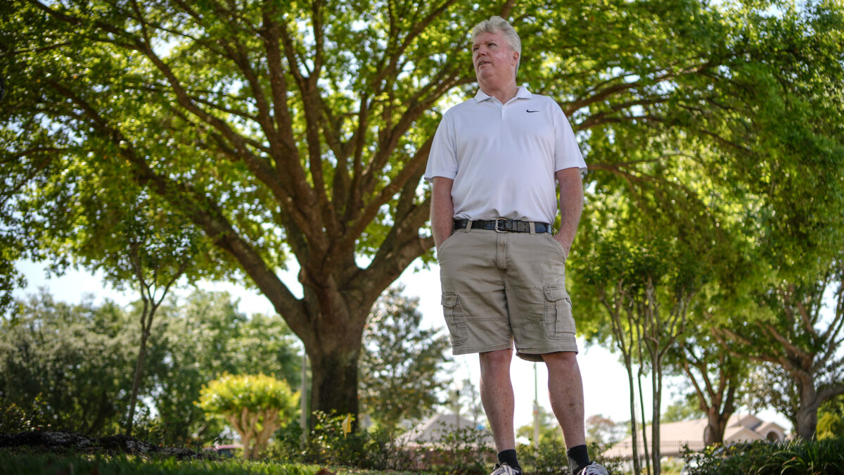 A photo of a man standing outside under a shaded canopy of trees.